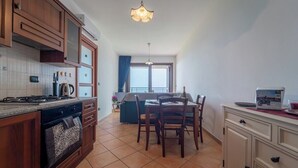 A kitchen with wooden cabinets, a stove, and a dining area with chairs and a table. - The Terrace on the Gulf of Alghero 2 (Alghero)