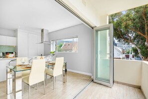 Une cuisine moderne avec un coin repas, une grande fenêtre et un balcon offrant une vue sur les immeubles et les arbres.
