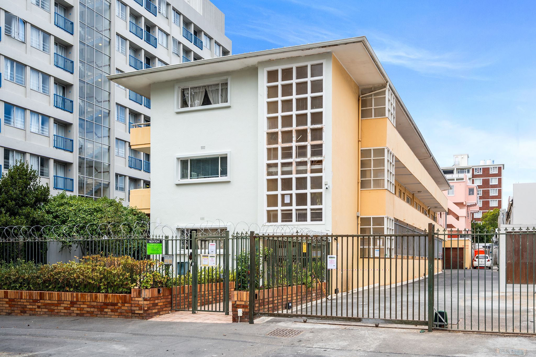 A modern building with a white and yellow facade, large windows, and a gated entrance.