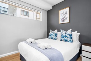 A modern bedroom with a large bed, a window, and a framed plant on the wall. - Vernor Court 4 (Cape Town)