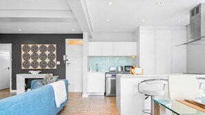 Una cocina moderna con armarios blancos, lavavajillas de acero inoxidable y una isla de vidrio con taburetes de bar.