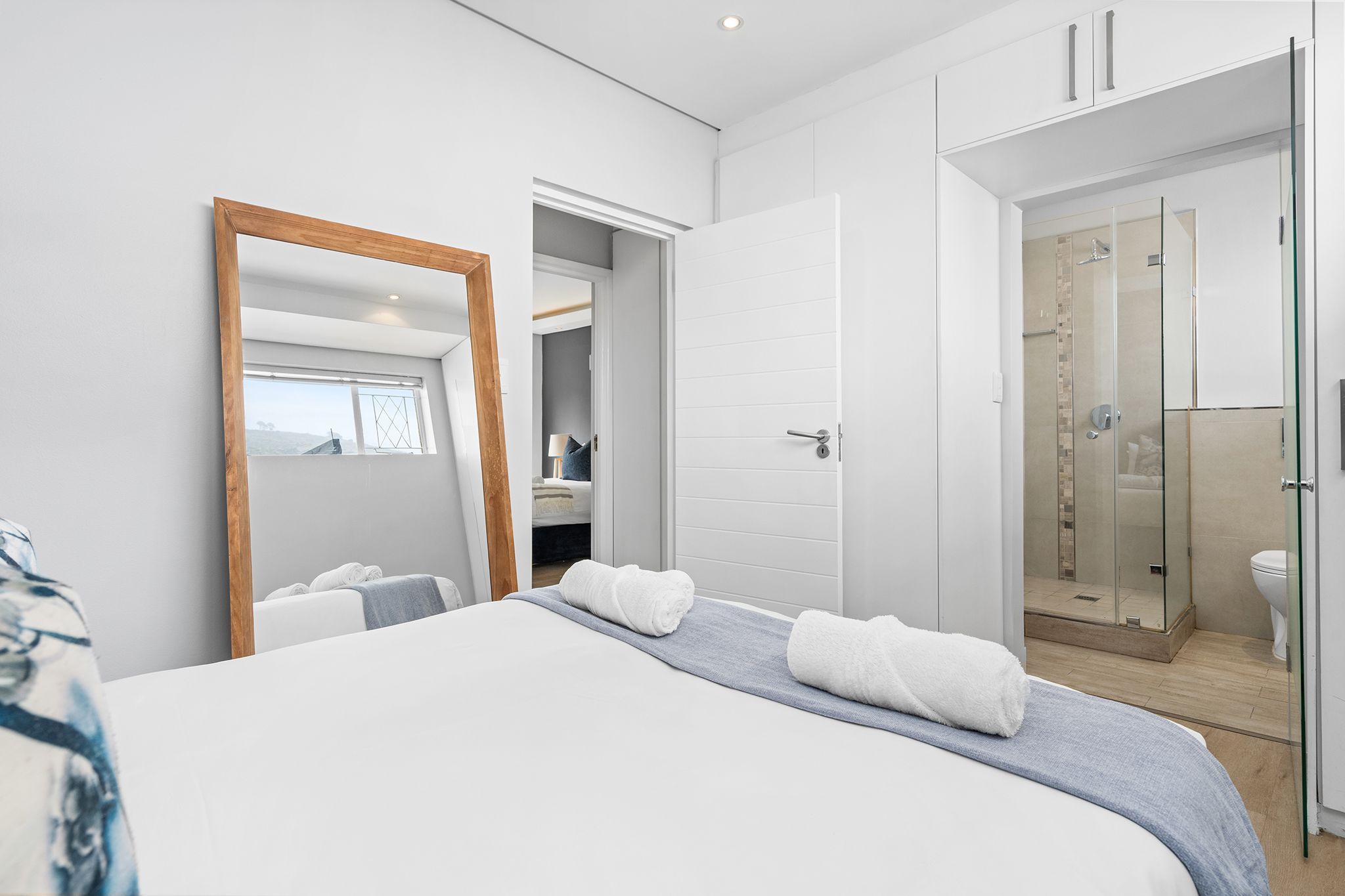Un dormitorio moderno con una cama grande, un vestidor amplio y una zona de ducha con paredes de vidrio.