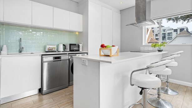 Una cocina moderna con armarios blancos, electrodomésticos de acero inoxidable y una isla central con taburetes de bar.