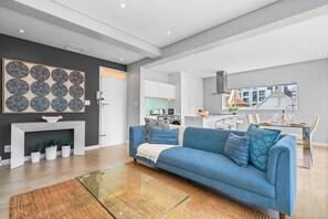 Un salon moderne avec un canapé bleu, une cheminée et une cuisine en arrière-plan.