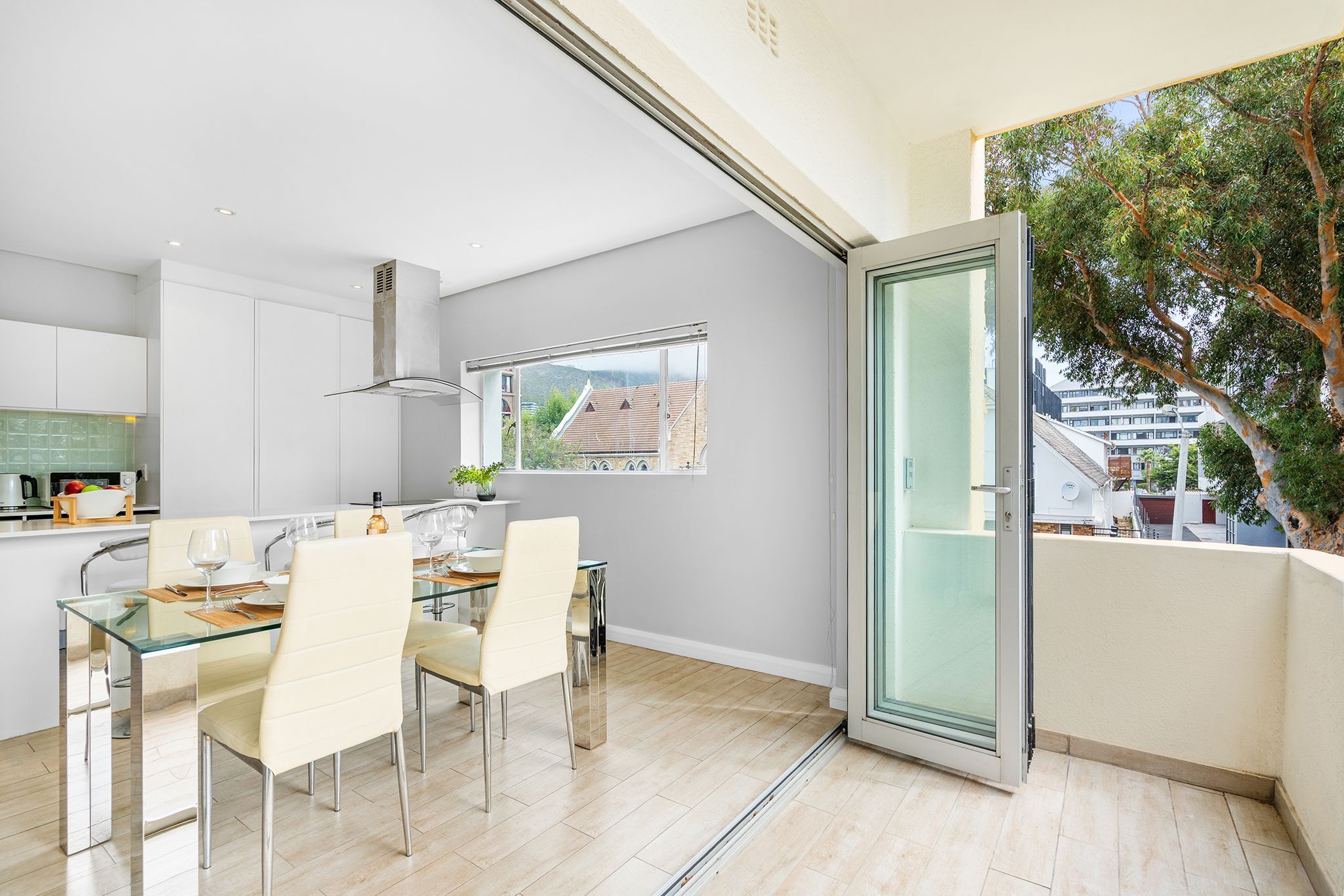 Eine moderne Küche mit Essbereich, großen Fenstern und einem Balkon mit Blick auf Gebäude und Bäume.