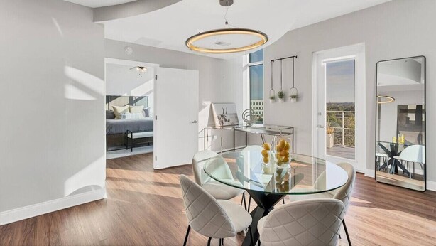 Ein modernes Interieur mit einem Glastisch, weißen Stühlen und Blick auf eine Stadtlandschaft durch große Fenster.