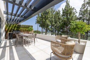 Eine Terrasse im Freien mit Grill, Esstisch, Stühlen und Blick auf Bäume und Gebäude.