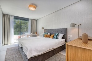 Ein modernes Schlafzimmer mit einem großen Bett, einem Schreibtisch und Blick ins Freie.