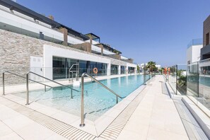 A swimming pool with glass railings, a stone wall, and modern buildings in the background. - Luxury vacation with a terrace and private pool (Marbella)