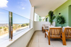 A balcony with a view of a landscape, a sofa, a table, and a potted plant. - Ipanema 2-Bedroom Apartment with a View (Mijas)