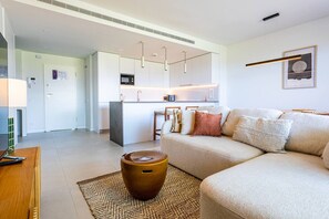 A modern living room with a sofa, a coffee table, and a kitchen area in the background. - Ipanema 2-Bedroom Apartment with a View (Mijas)