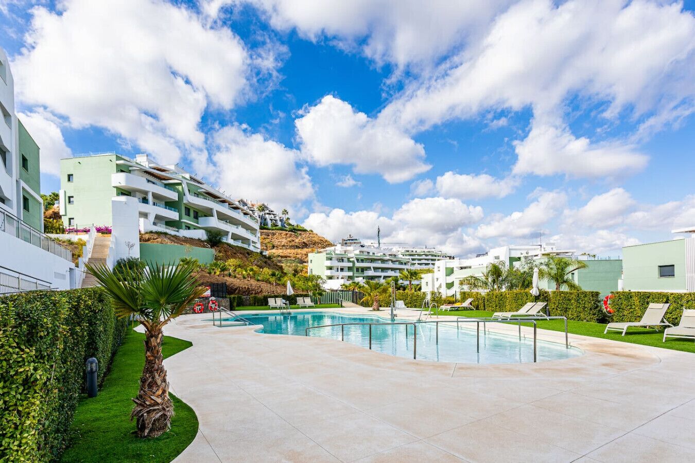 A modern hotel with a swimming pool, sun loungers, and a view of the surrounding buildings.