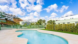 A swimming pool with a curved edge, surrounded by a low fence and greenery. - Ipanema 2 BR apartment with views (Mijas)