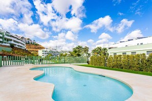 A swimming pool with a curved edge, surrounded by a low fence and greenery. - Ipanema 2 BR apartment with views (Mijas)