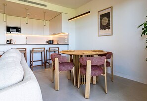 A modern kitchen with built-in appliances, a dining area with a round table and patterned chairs, and a minimalist living space with a sofa. - Ipanema 2-Bedroom Apartment with a View (Mijas)