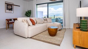 A modern living room with a sectional sofa, a small wooden table, a floor lamp, and a large window with a view. - Ipanema 2 BR apartment with views (Mijas)
