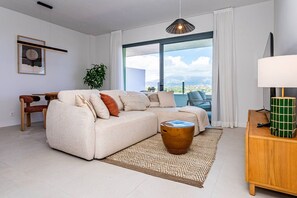A modern living room with a sectional sofa, a small wooden table, a floor lamp, and a large window with a view. - Ipanema 2 BR apartment with views (Mijas)