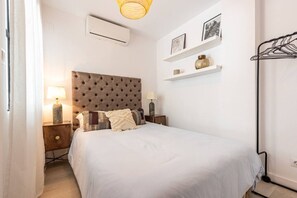 A bedroom with a bed, nightstands, a wall-mounted air conditioner, and a shelf with decorative items. - Modern ground-floor apartment with a private garden in Nueva Andalucía (Marbella)