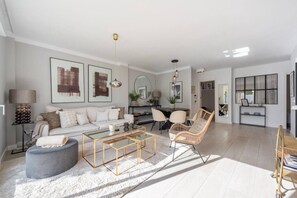 A modern living room with a sofa, coffee table, and chairs, a dining area with a table and chairs, and a kitchen area with a window. - Modern ground-floor apartment with a private garden in Nueva Andalucía (Marbella)