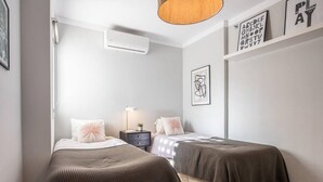 A bedroom with two beds, a bedside table with a lamp, and a wall-mounted air conditioner. - Modern ground-floor apartment with a private garden in Nueva Andalucía (Marbella)