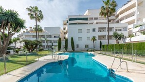 A swimming pool with a clear blue water surface, surrounded by a paved deck and a low fence. - Modern ground-floor apartment with a private garden in Nueva Andalucía (Marbella)