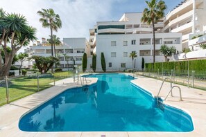 A swimming pool with a clear blue water surface, surrounded by a paved deck and a low fence. - Modern ground-floor apartment with a private garden in Nueva Andalucía (Marbella)