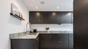 A modern kitchen with dark cabinetry, a granite countertop, and a stainless steel range hood. - Modern ground-floor apartment with a private garden in Nueva Andalucía (Marbella)