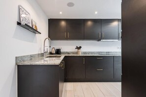 A modern kitchen with dark cabinetry, a granite countertop, and a stainless steel range hood. - Modern ground-floor apartment with a private garden in Nueva Andalucía (Marbella)