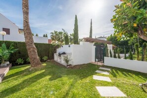 A well-maintained garden with a white wall, a barbecue area, and a pathway leading to a gate. - Modern ground-floor apartment with a private garden in Nueva Andalucía (Marbella)