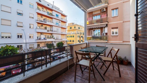 Un balcone con tavolo e sedie, vista su un panorama urbano con edifici a più piani.