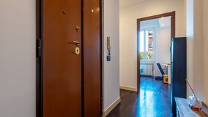 Un corridoio con una porta in legno, un telefono e vista su una stanza con finestra e termosifone.