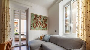 Una stanza con un divano grigio, un quadro appeso al muro e una vista attraverso una porta in vetro.