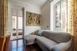 A room with a grey sofa, a painting on the wall, and a view through a glass door. - Domus Oleandri - WelcometoRhome (Rome)
