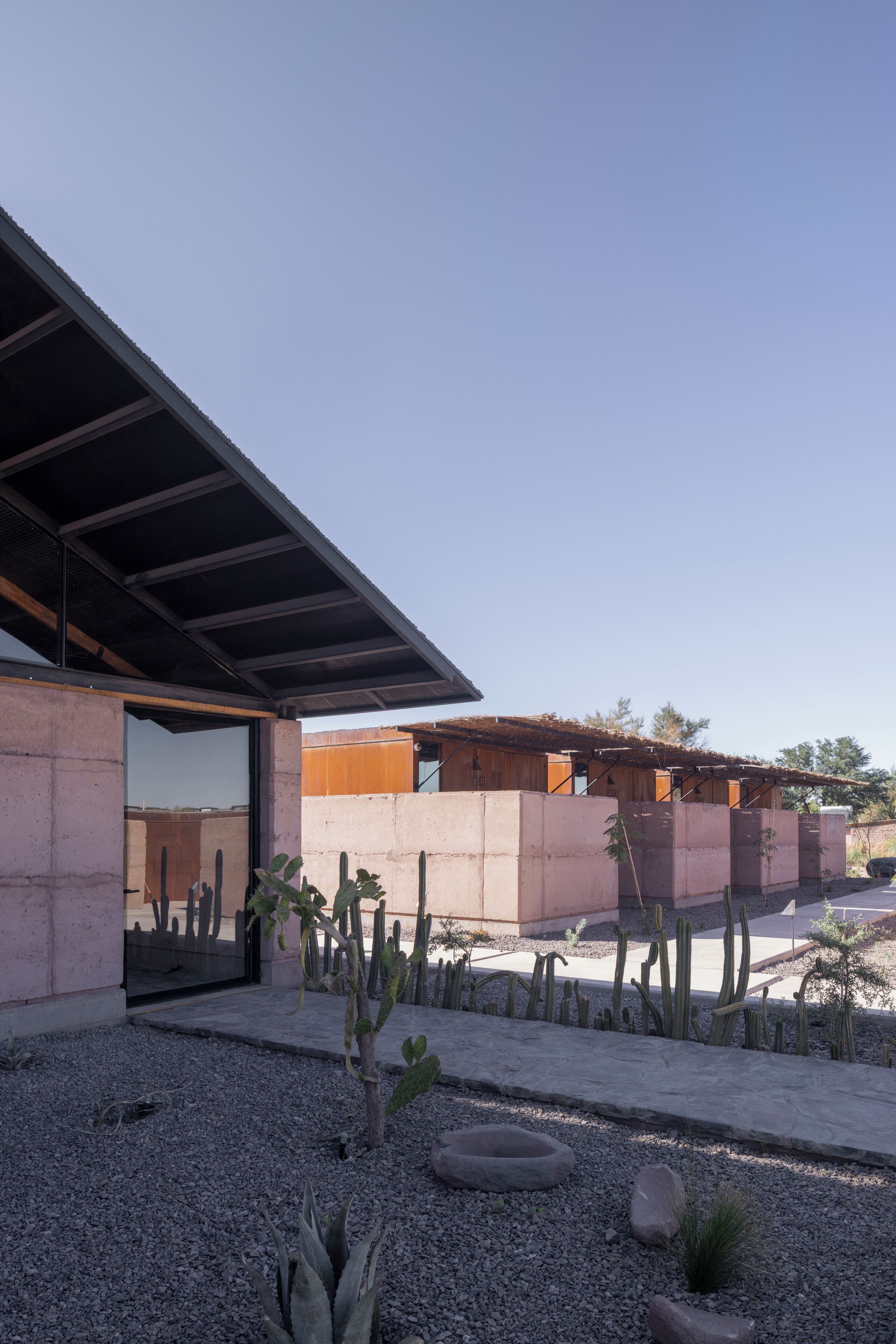 Un edificio moderno con fachada de concreto, puerta de vidrio y un patio con cactus y rocas.