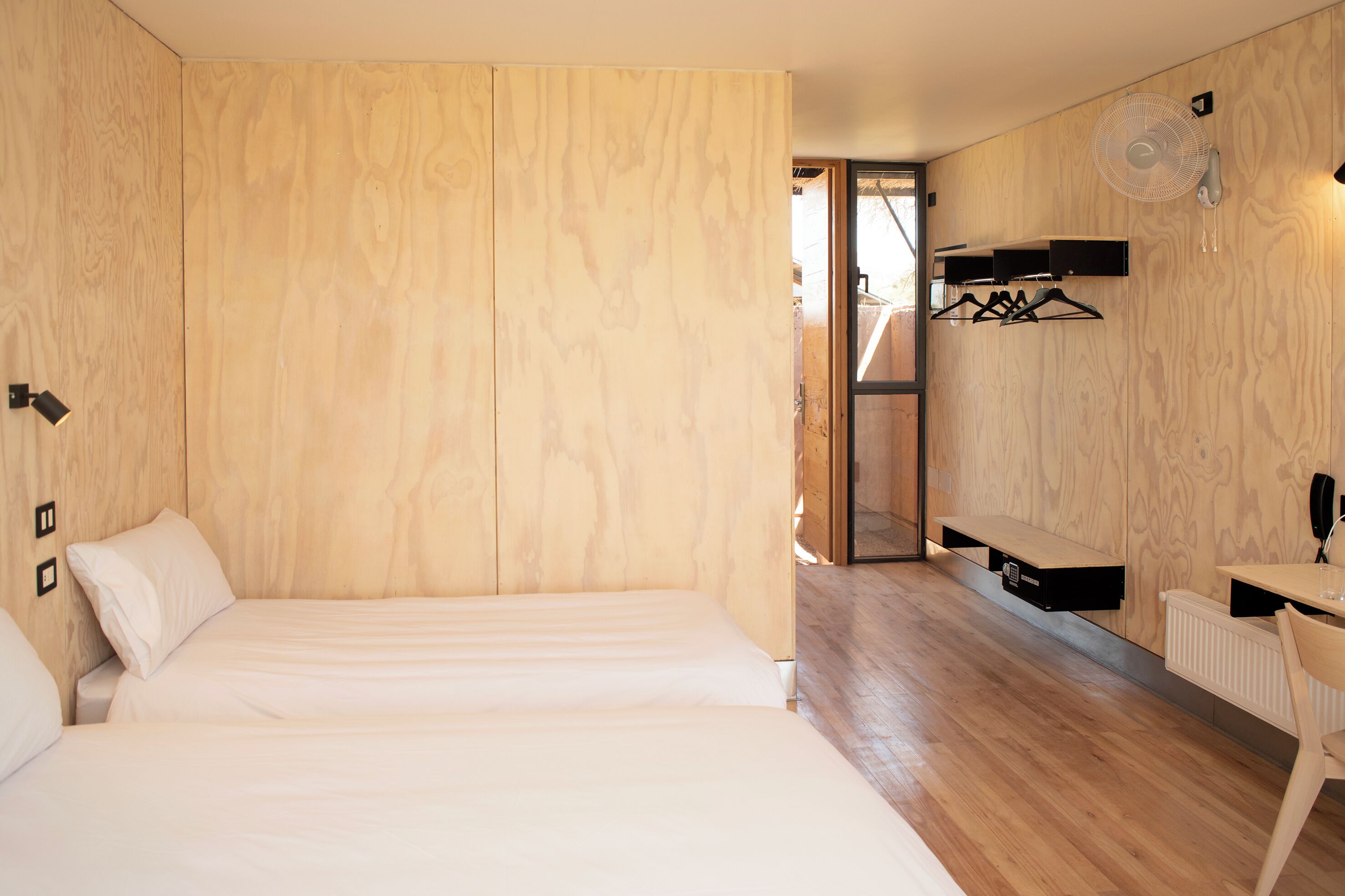 A bedroom with a wooden wall, a bed, a desk with a chair, and a hanging clothes rack.