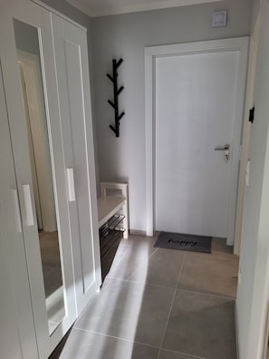 A hallway with a white door, a black coat rack, a small white table, and a 'happy' mat on the floor.