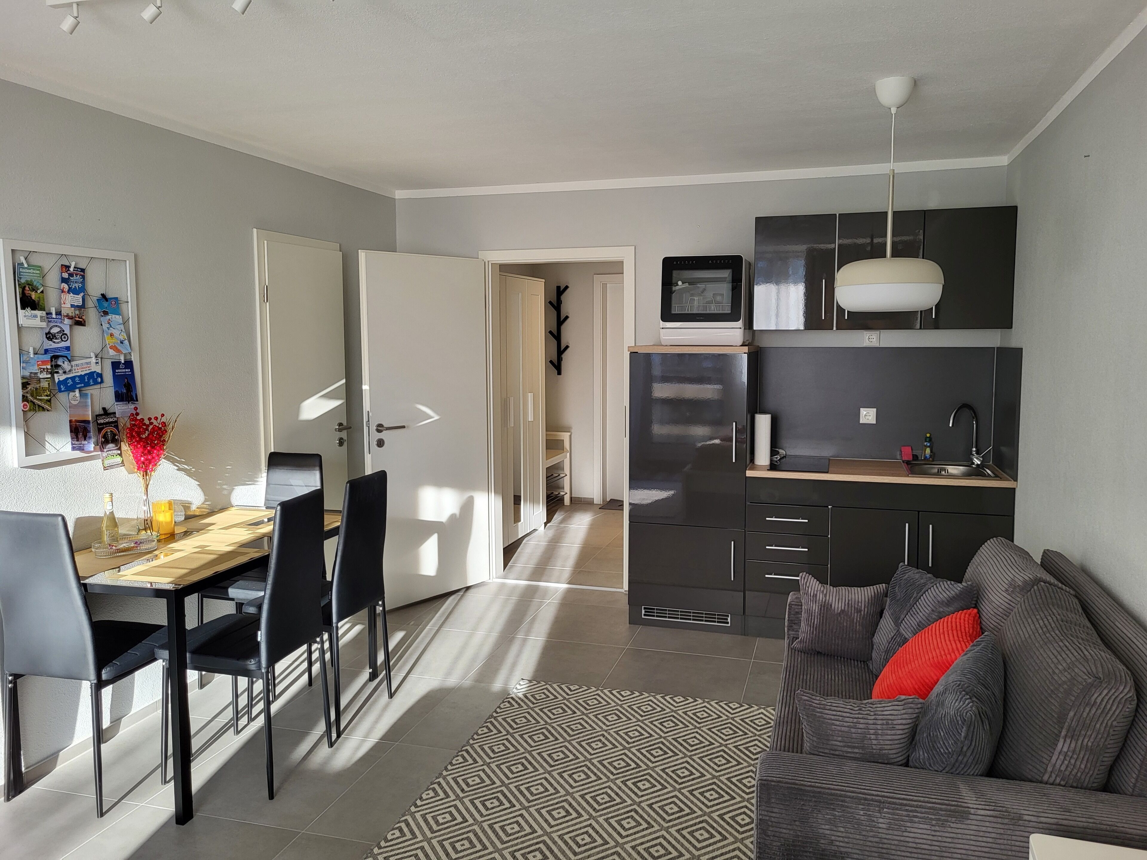 Una cucina moderna con mobili scuri, forno integrato e microonde. C'è una zona pranzo con un tavolo e sedie in legno, e un tappeto a motivi sul pavimento.