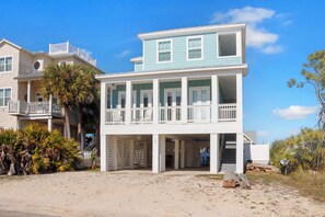 Una casa fronte spiaggia su due piani, con un balcone, un garage coperto e un vialetto in sabbia.