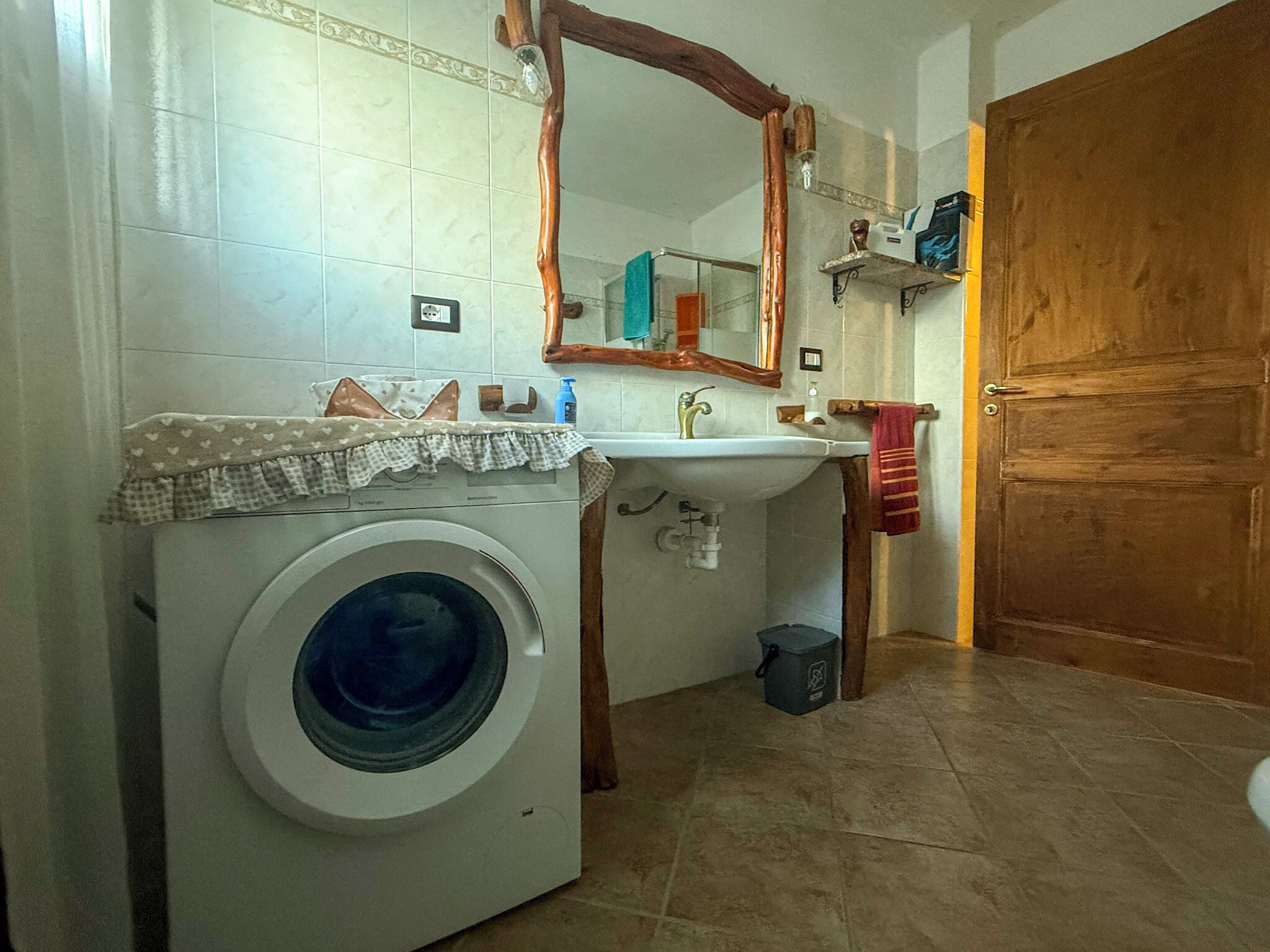 A compact bathroom with a washing machine, a sink, and a wooden door.