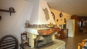 A kitchen with a stone hearth, wooden chairs, a wooden table, and a refrigerator. - L'ulivo (Portoscuso)
