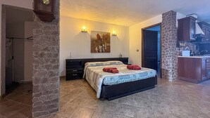 A bedroom with a bed, a nightstand, a painting, and a stone wall. - L'ulivo (Portoscuso)