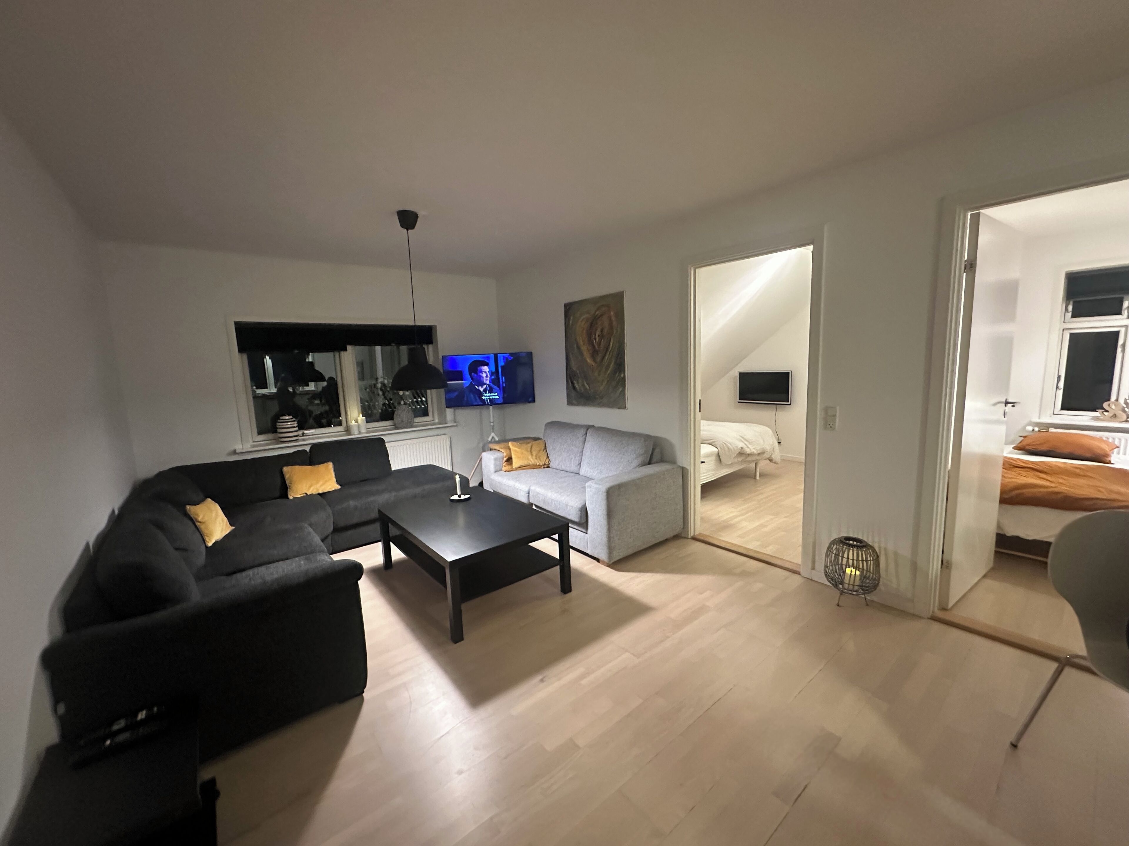 Un salon moderne avec un canapé noir, un canapé blanc et une table basse. Un téléviseur à écran plat est fixé au mur, et un tableau est accroché au-dessus du canapé blanc.