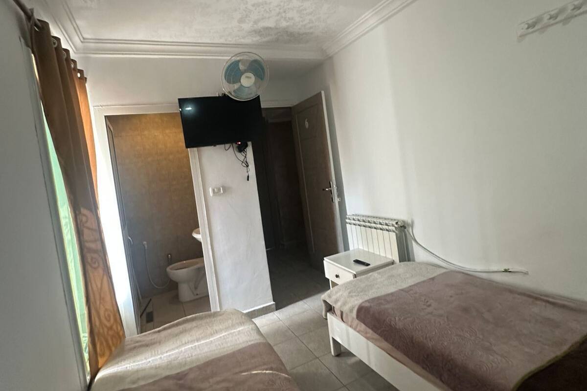 Une chambre d’hôtel avec deux lits, un ventilateur de plafond, une télévision et une salle de bain visible à travers une porte ouverte.