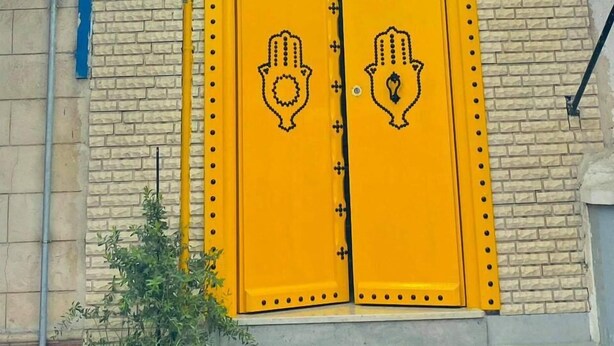L'ingresso di un hotel con una insegna in arabo e inglese, due porte gialle con motivi decorativi e un muro in mattoni.