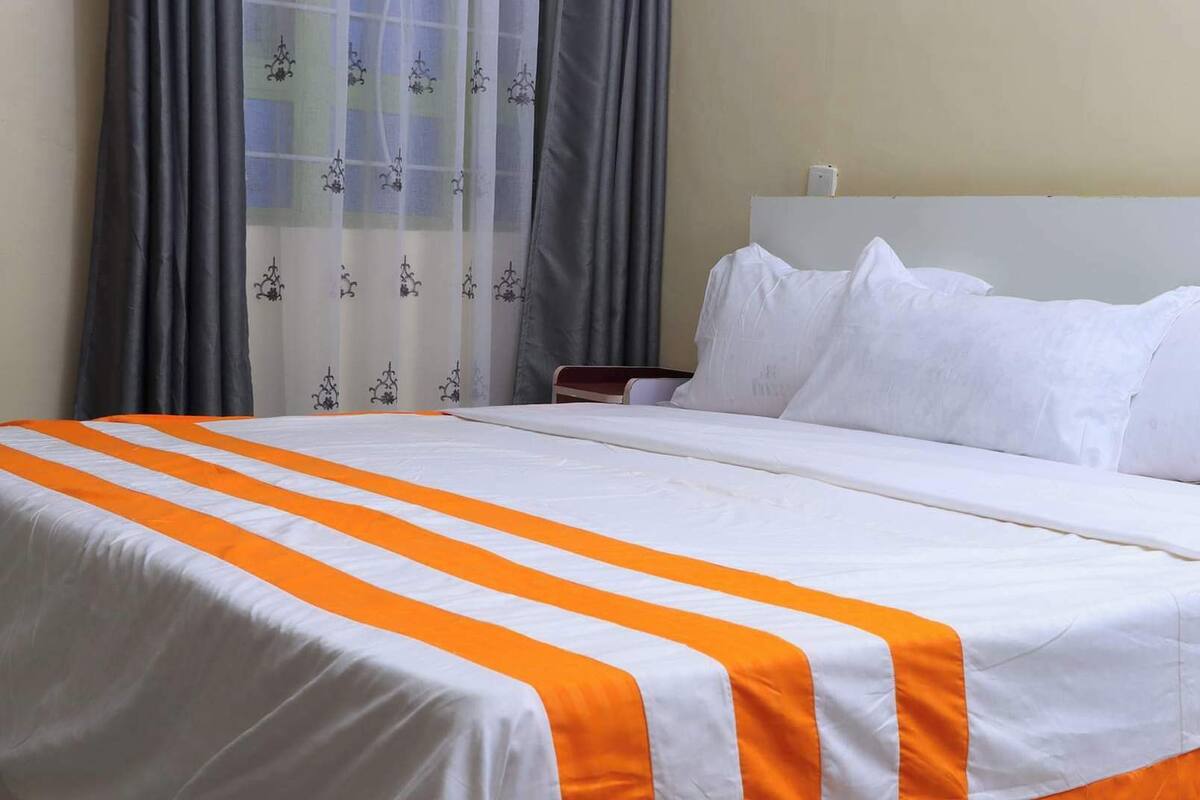 A hotel room with a bed, white bedding, and a striped orange and white bedspread.