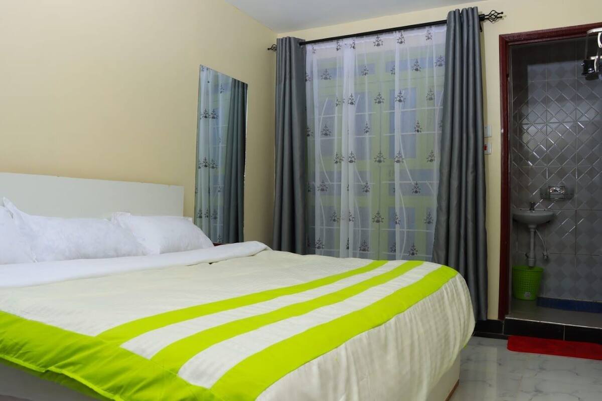 A hotel room with a bed, curtains, a bathroom with a sink, and a door.