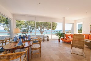 A spacious room with a large dining table, wicker chairs, and a sofa with orange cushions. - Villa with pool and spectacular see views near the beach (Begur)