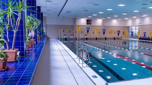 An indoor swimming pool with lanes, starting blocks, and potted plants along the sides.