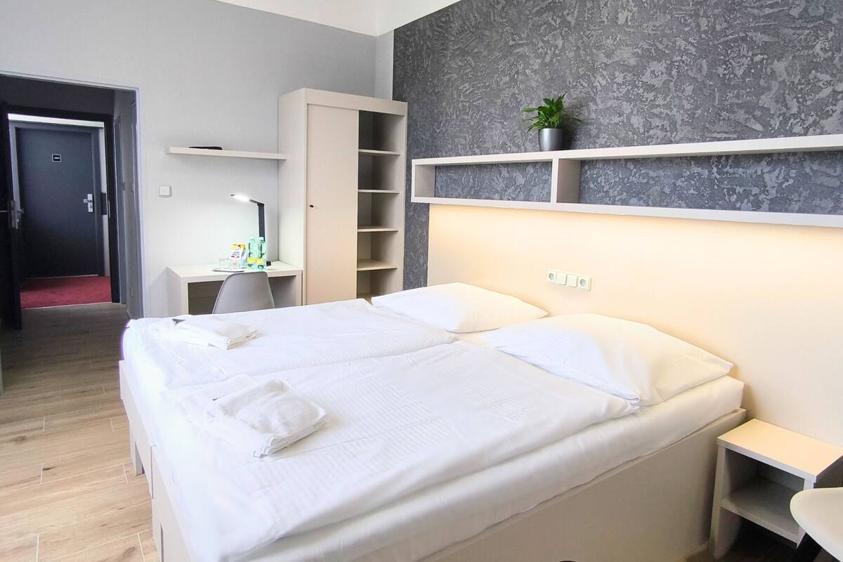 Una habitación de hotel moderna con cama, mesitas de noche, escritorio y armario.