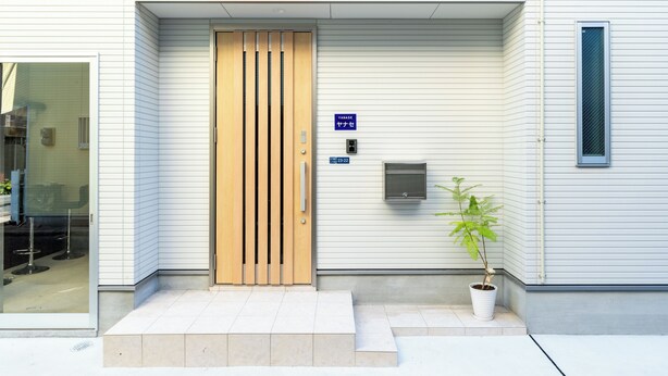 Una entrada de edificio con puerta de madera, planta en maceta y un cartel que indica la entrada.